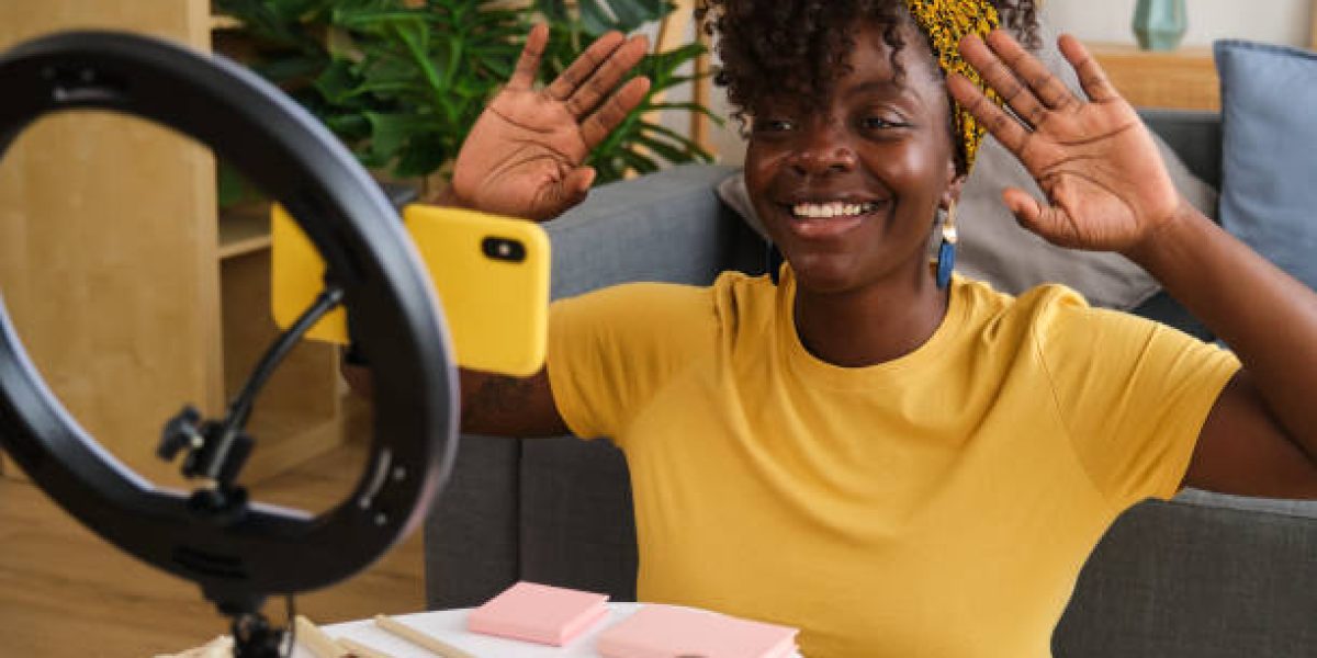 Smiling beauty influencer waving while recording a makeup tutorial using a ring light and a smartphone